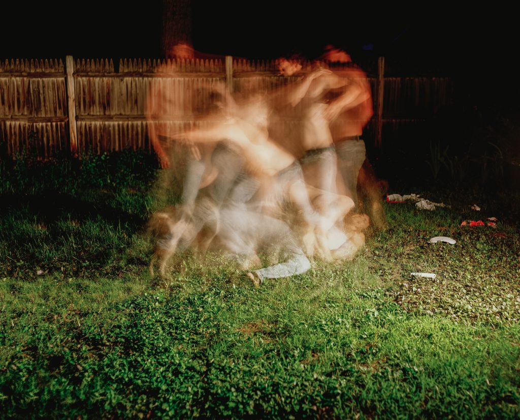 Time lapse of two men wrestling in a backyard with a wooden fence behind them