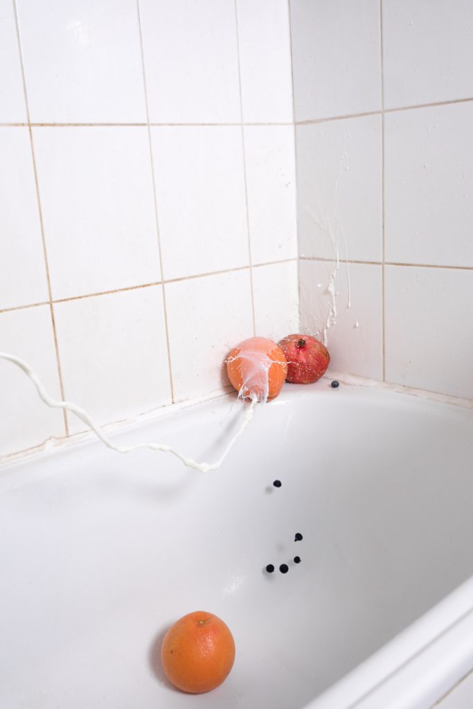 Milk splash on orange and pomegranate in a bathub with blueberries